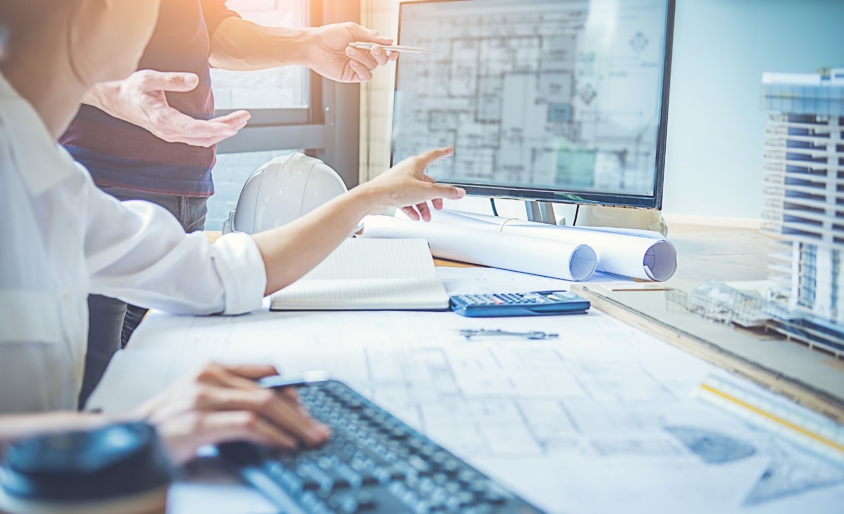 Zwei Bauchzeichner/Ingenieure besprechen sich wegen einem Projekt, währenddessen sie am Computer arbeiten.