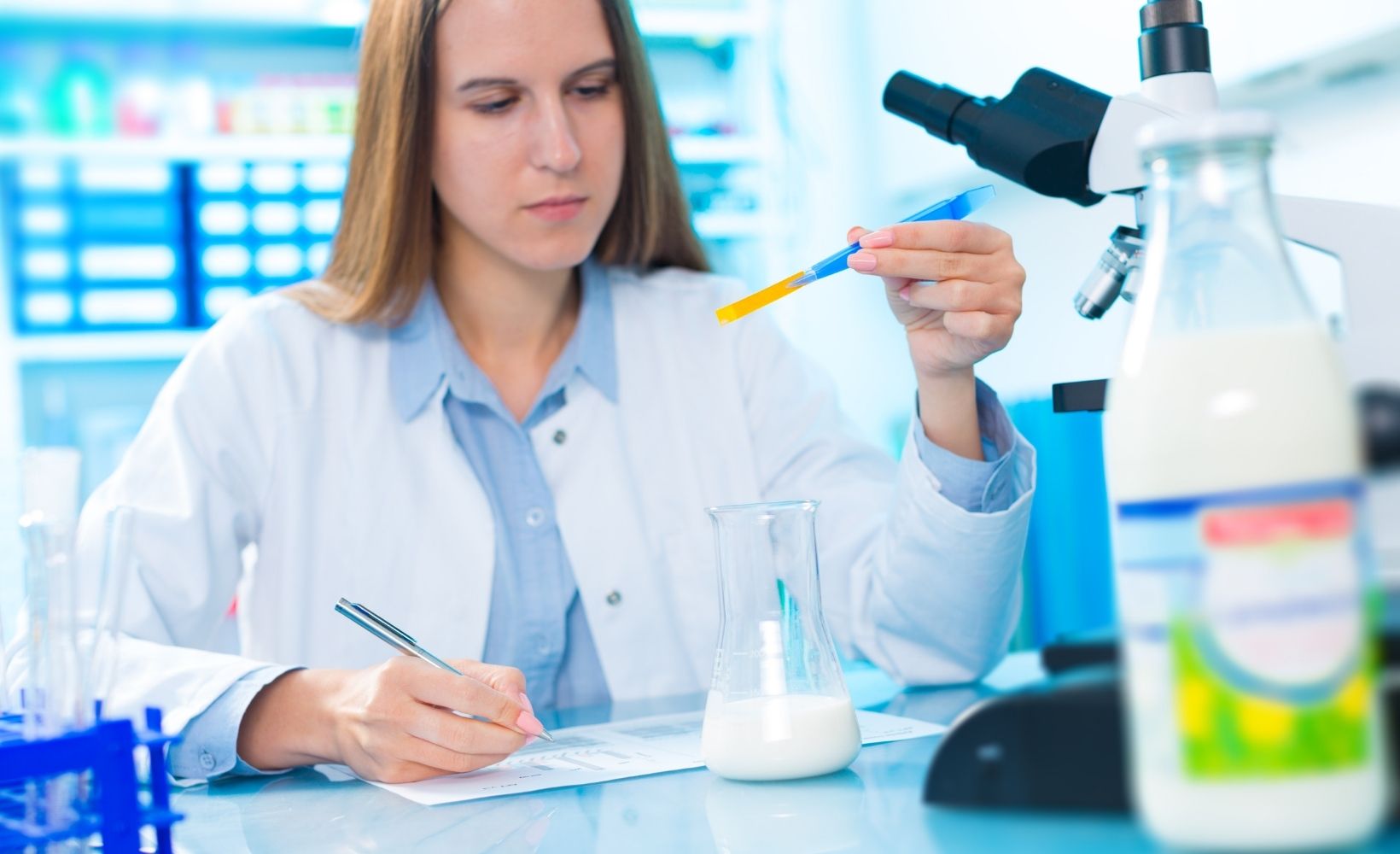 Eine Milchwirtschaft Laborantin testet im Labor eine Milch mit einem Werkzeug und notiert die Ergebnisse.