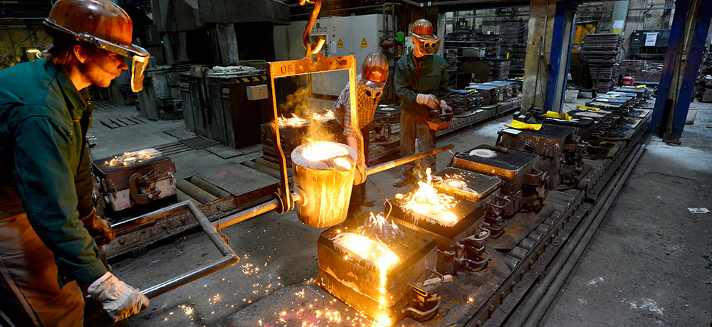 Industrie mit drei Verfahrenstechnologen, die brennendes Metall auf Platten gießen.
