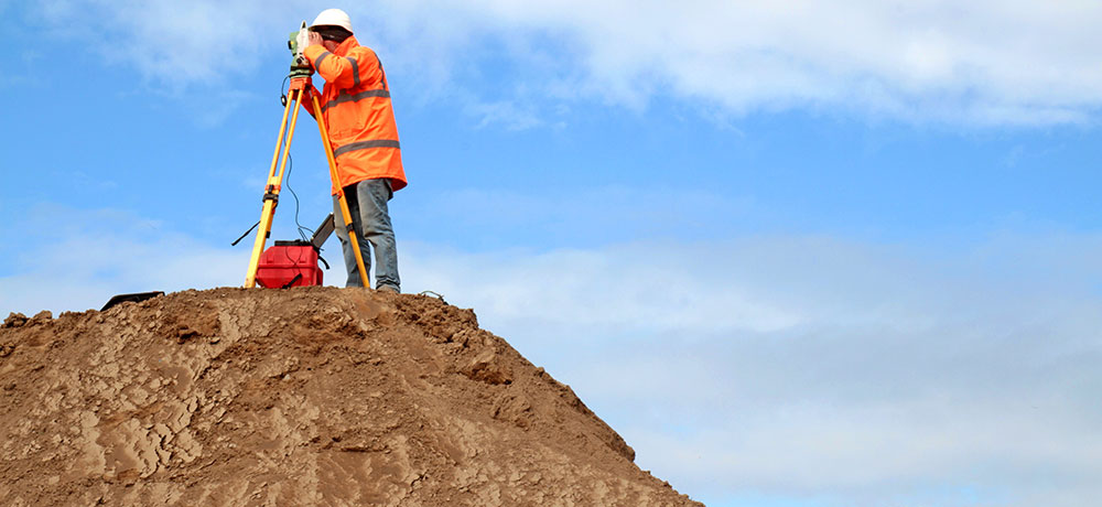 Vermessungstechniker steht auf einem Berg und vermesst diesen mit seinen Werkzeugen.
