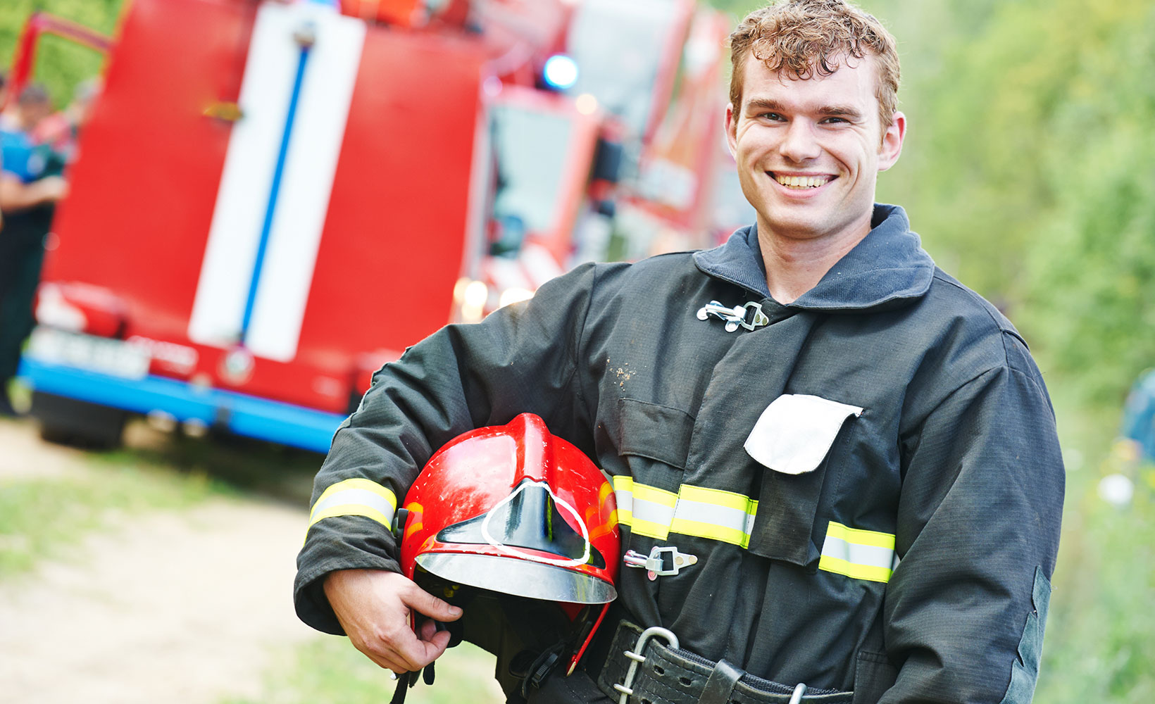 Feuerwehrmann lächelt in die Kamera und hält seinen Helm unter seinem rechten Arm.