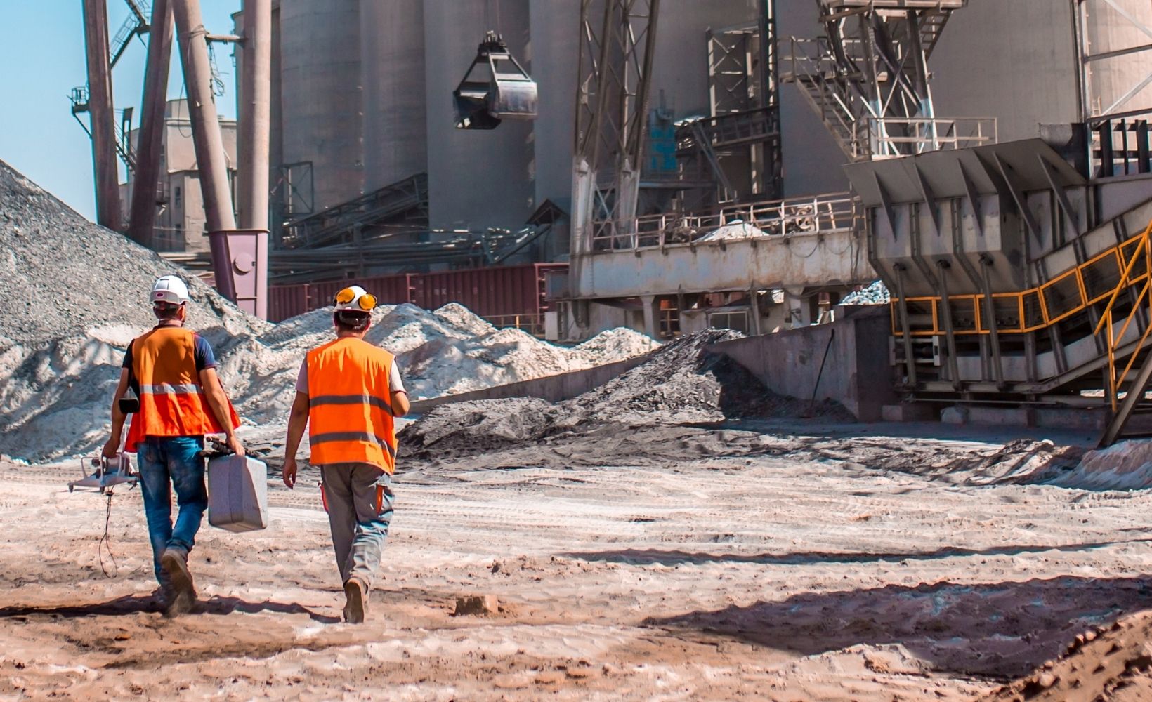 Zwei Aufbereitungsmechaniker laufen auf eine Baustelle mit diversen Werkzeugen zu und tragen ihre Schutzkleidung.