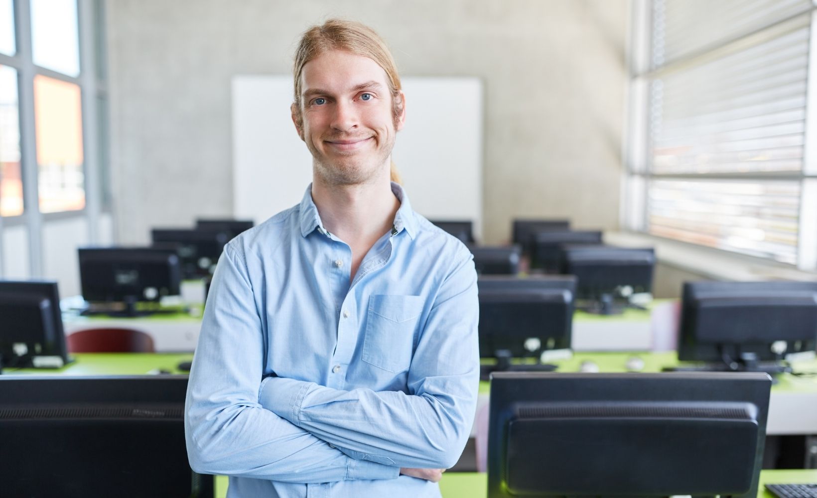 Fachinformatiker lächelt in die Kamera. Im Hintergrund ein Großraumbüro.