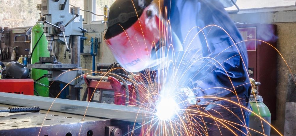 Fachkraft für Metalltechnik zersägt ein Metallstück in seiner Schutzkleidung.