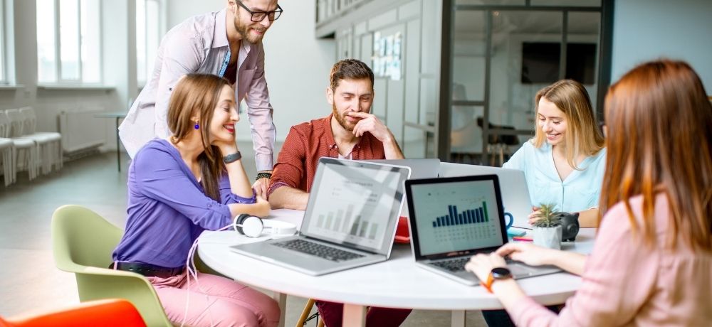 Team aus 5 sitzen in einem runden Tisch und analysieren Grafiken.