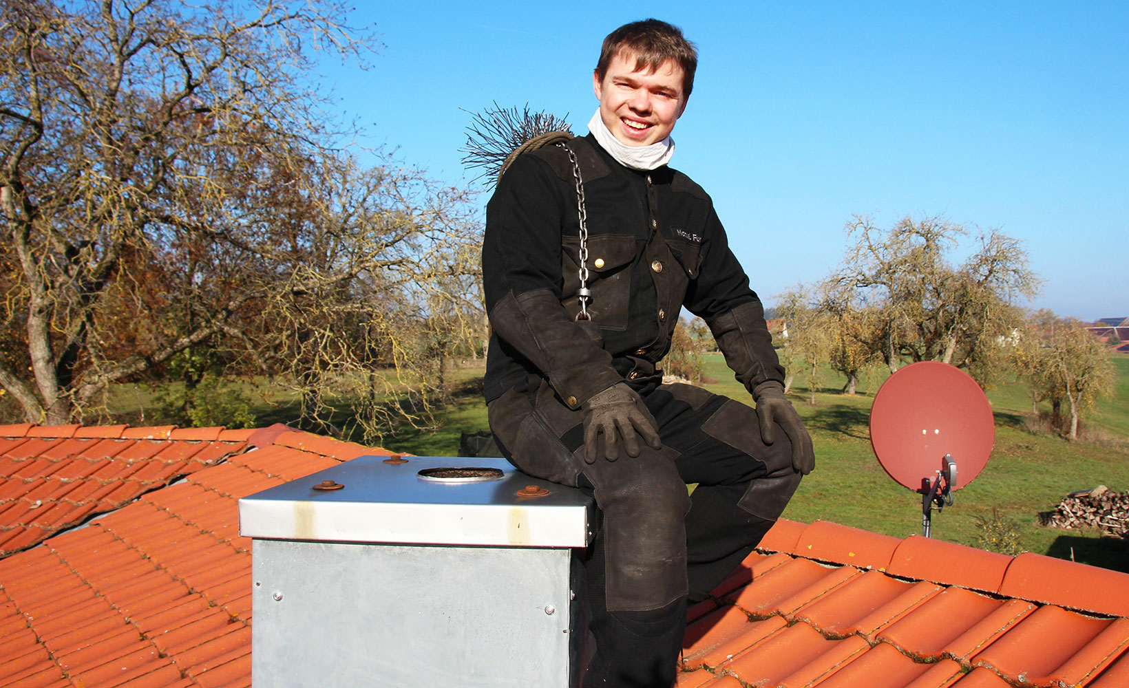 Schornsteinfeger sitzt auf dem Schornstein, oben auf dem Dach eines Hauses.