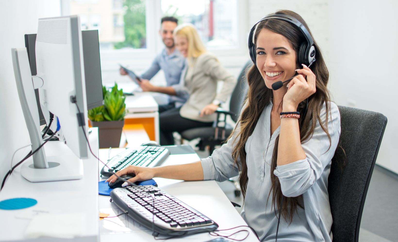Eine junge Frau sitzt mit Headset am Computer.