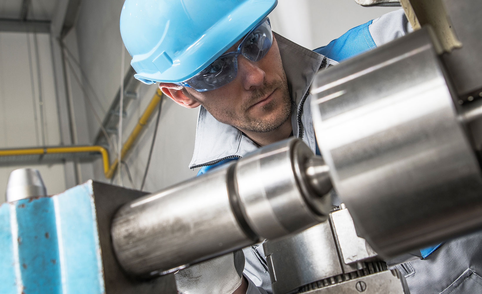 Ein Werkzeugmechaniker mit Helm, Schutzbrille und Handschuhen arbeitet an einer Maschine.