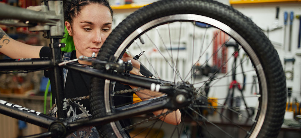 Eine Zweiradmechatronikerin tüftelt an einem Fahrrad.