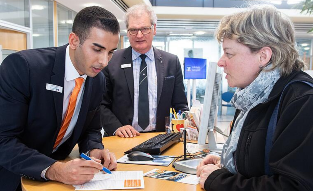 Unterlagen über eine Theke werden mit Angestellten und Kundin besprochen.