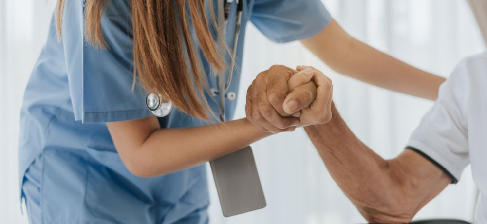 Altenpflegehelferin nimmt ältere Person an der Hand und hilft aufzustehen.