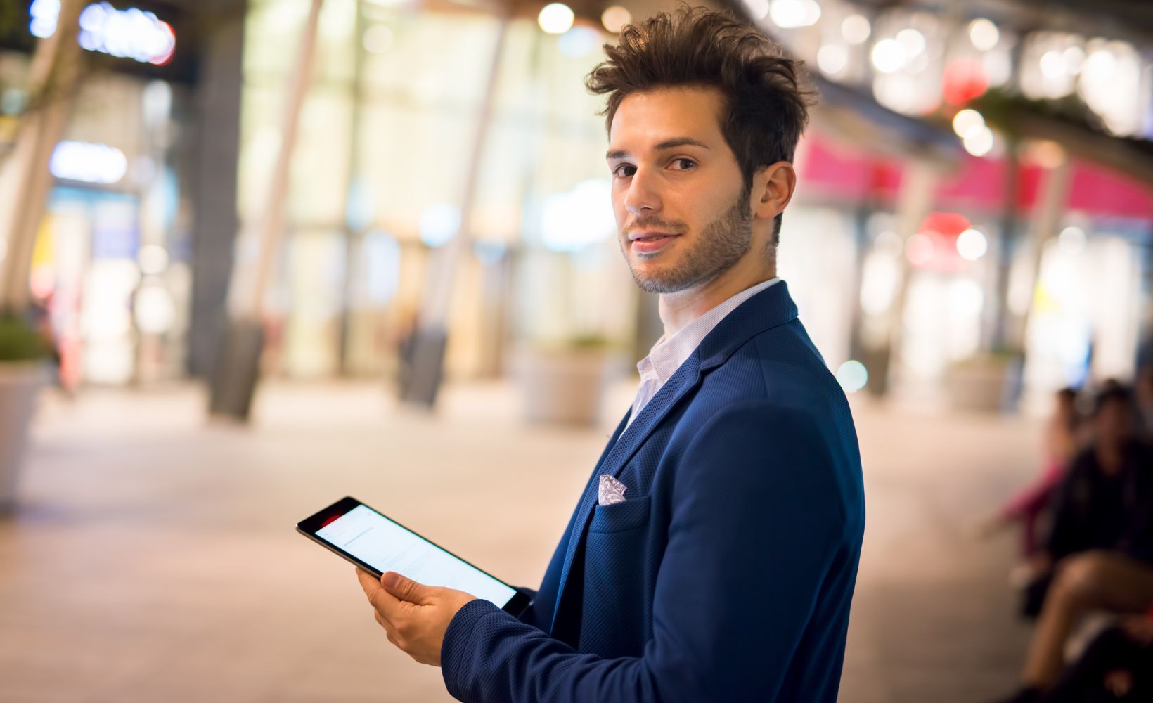 Dualer Student für Eventmanagement hält ein Tablet in der Hand und schaut in die Kamera.