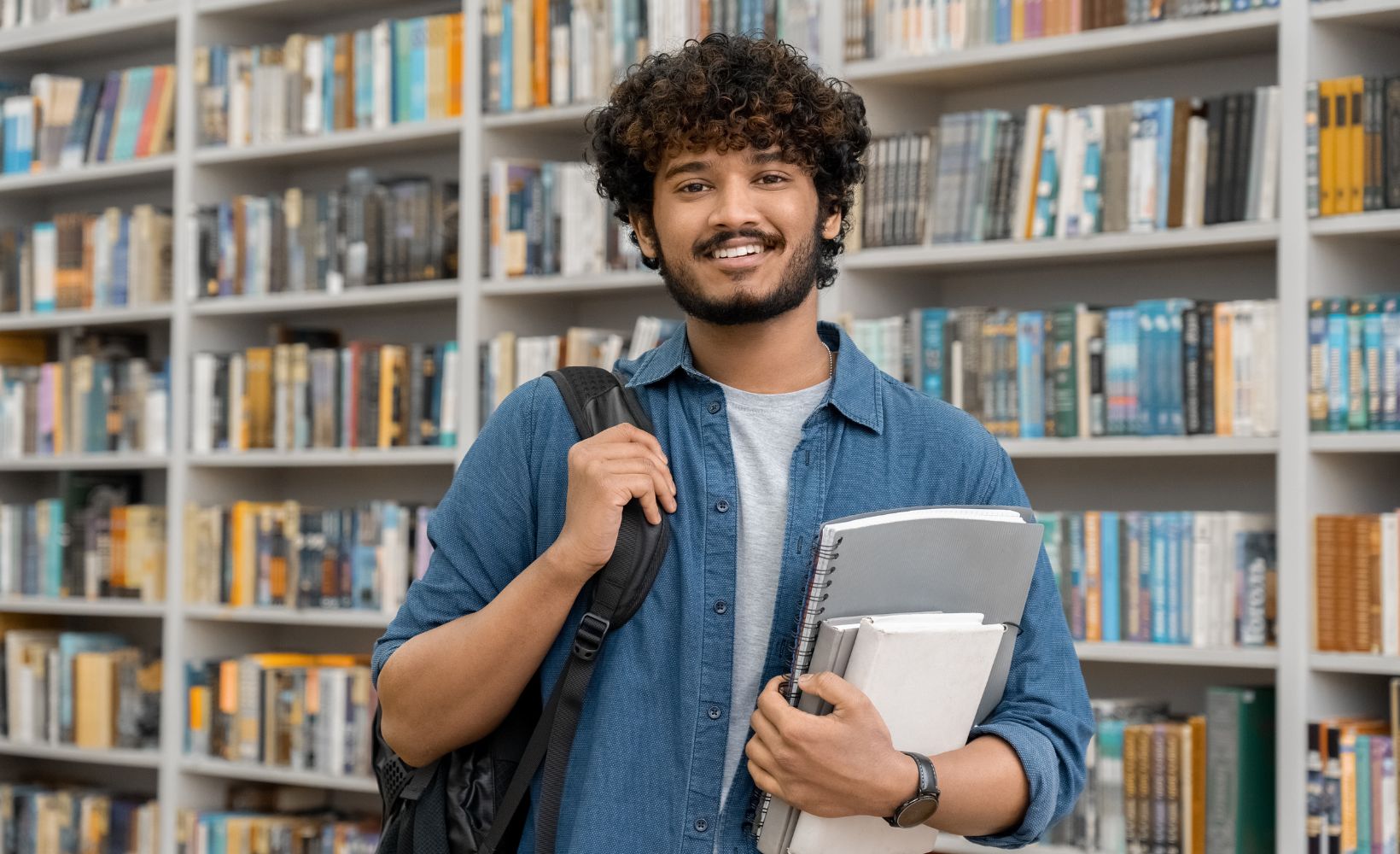 Dualer Student steht in der Bibliothek und lächelt in die Kamera.