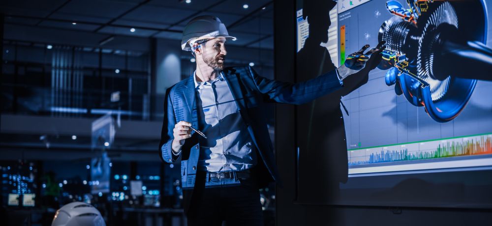Ingenieur mit Helm auf dem Kopf zeigt etwas Technisches am Projektor.