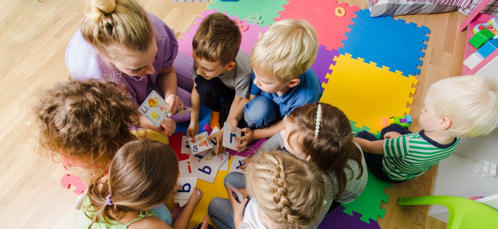 Sozialpädagogische Assistentin zeigt den Kindern die Buchstaben.
