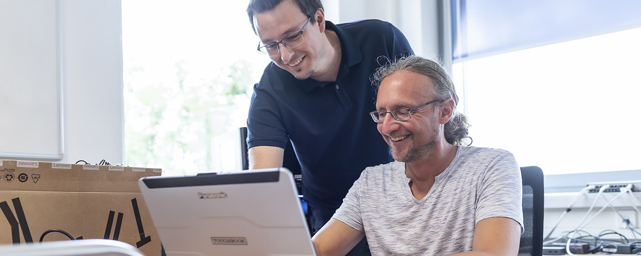 Zwei Mitarbeiter schauen sich etwas auf einem Laptop an.