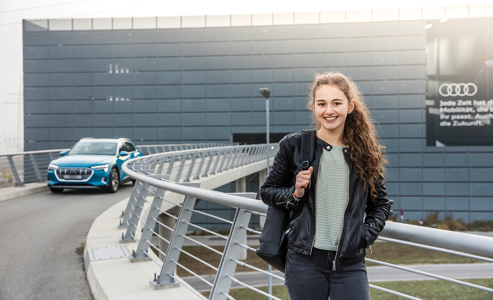 Junge Auszubildende steht vor dem AUDI-Parkhaus und lächelt