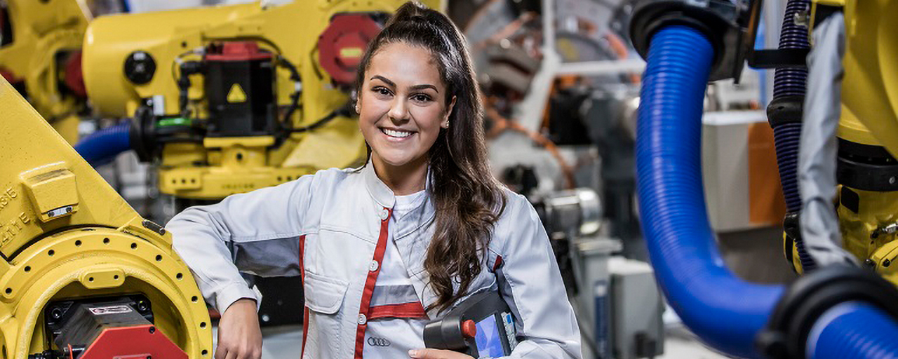 Audi Auszubildende lächelt und lehnt sich an einer Produktionsmaschine an