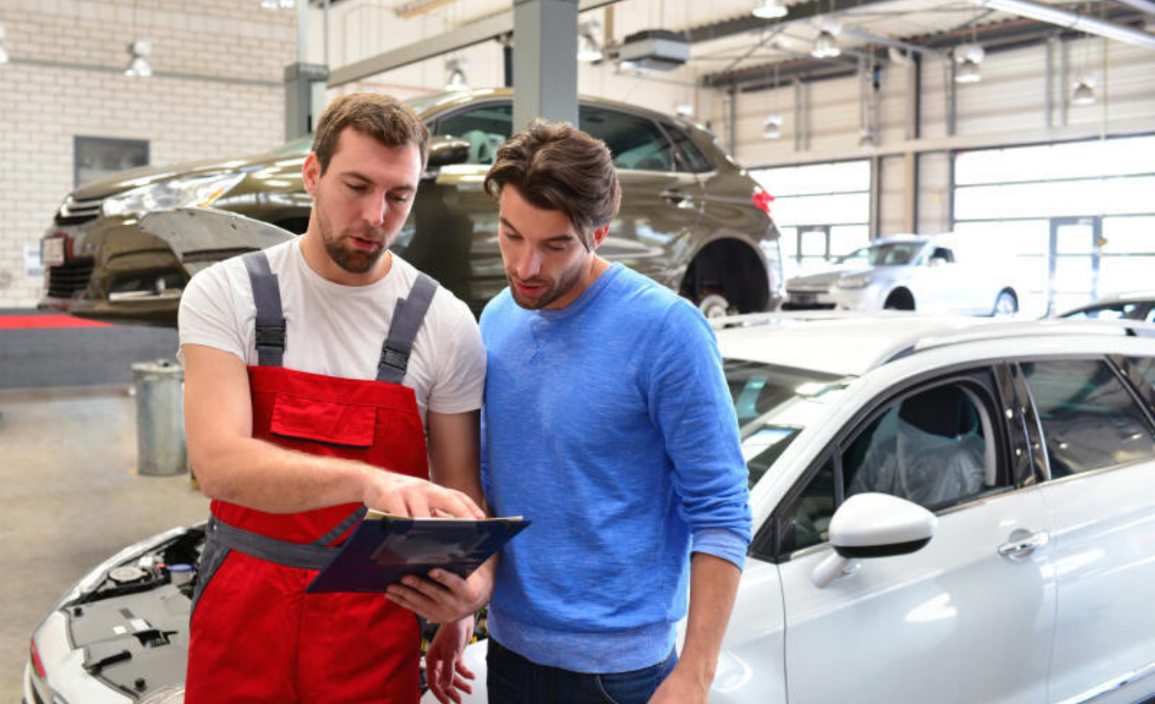 Zwei Kfz-Mechatroniker diskutieren in der Werkstatt einen Auftrag.