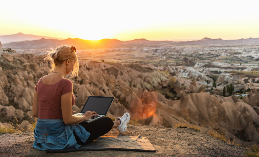 Eine junge Frau sitzt mir ihrem Laptop in der idyllischen Natur.