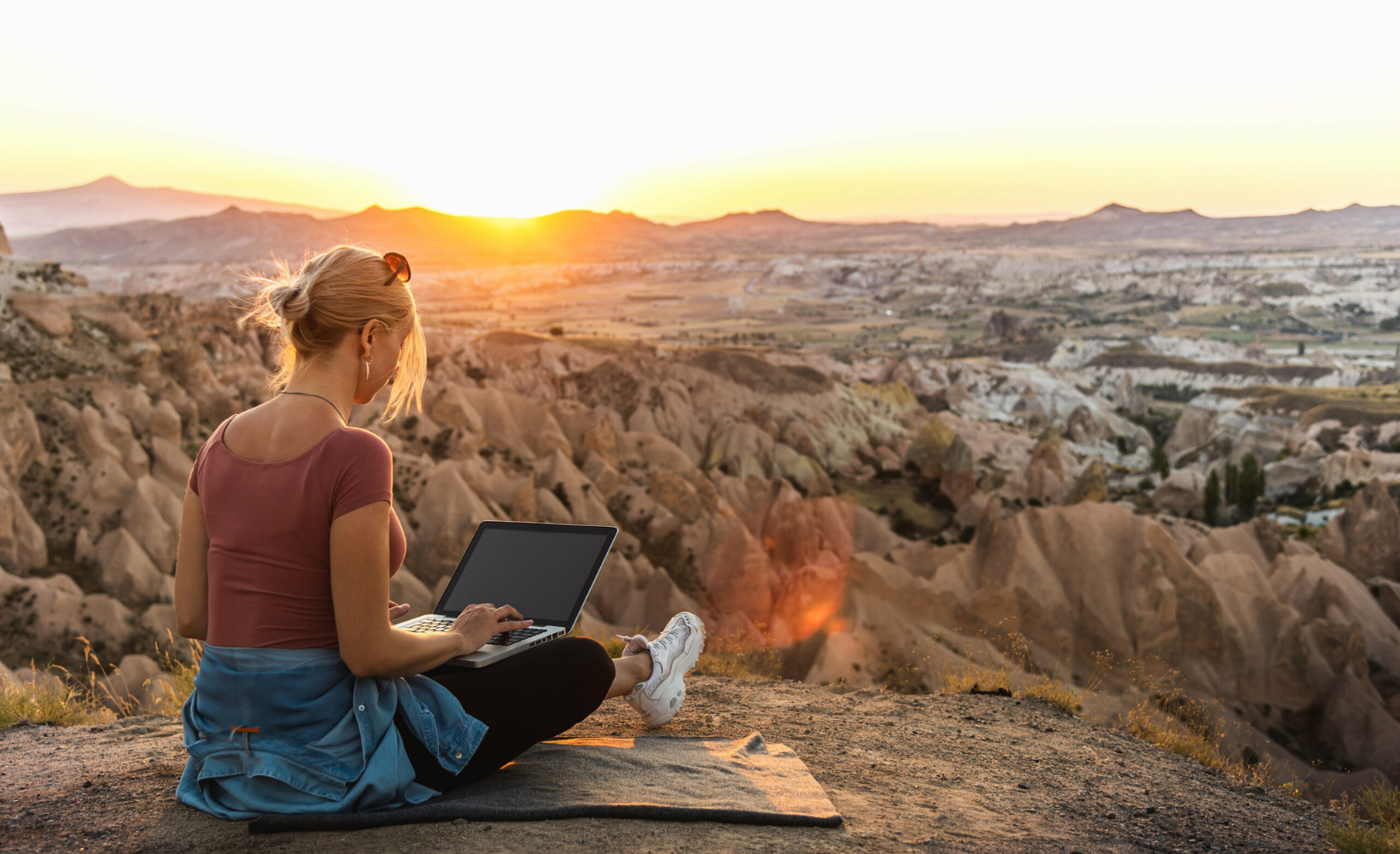 Eine junge Frau sitzt mir ihrem Laptop in der idyllischen Natur.