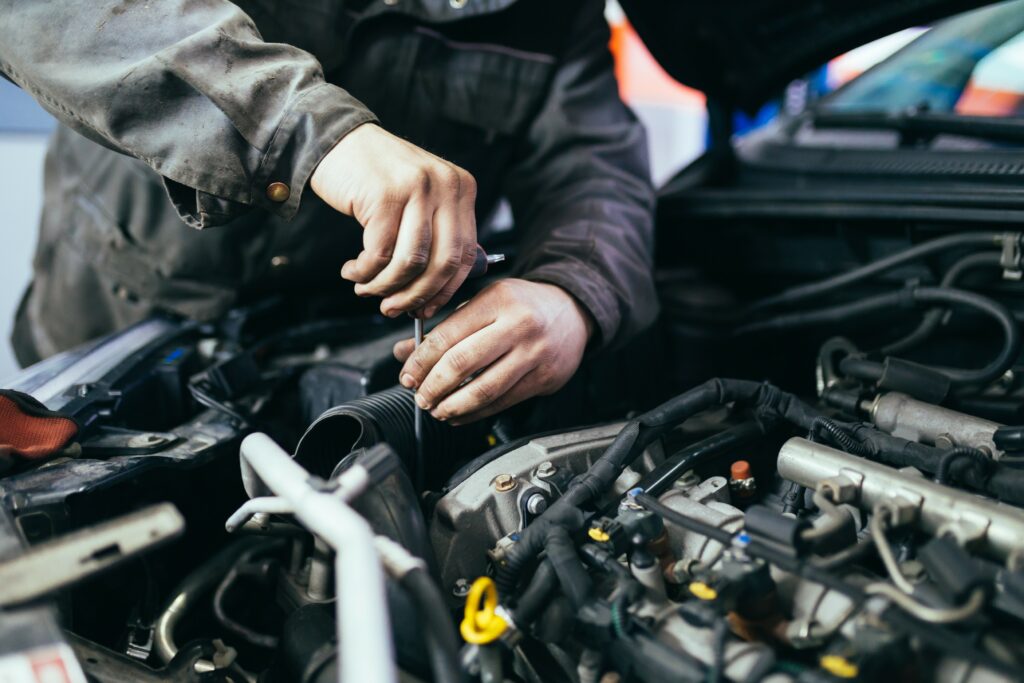 Ein Auszubildender im Handwerk arbeitet als Kfz-Mechatroniker an einem Automotor.