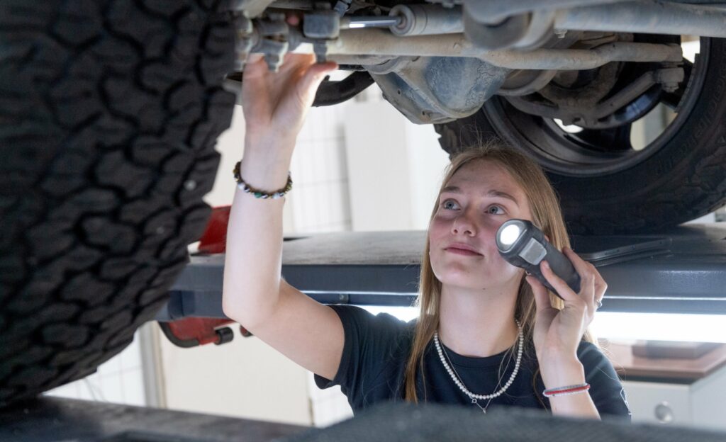 Melissa Schwab, Auszubildende zur Autmobilkauffrau bei Assenheimer + Mulfinger, untersucht in der Werkstatt die Unterseite eines Autos.