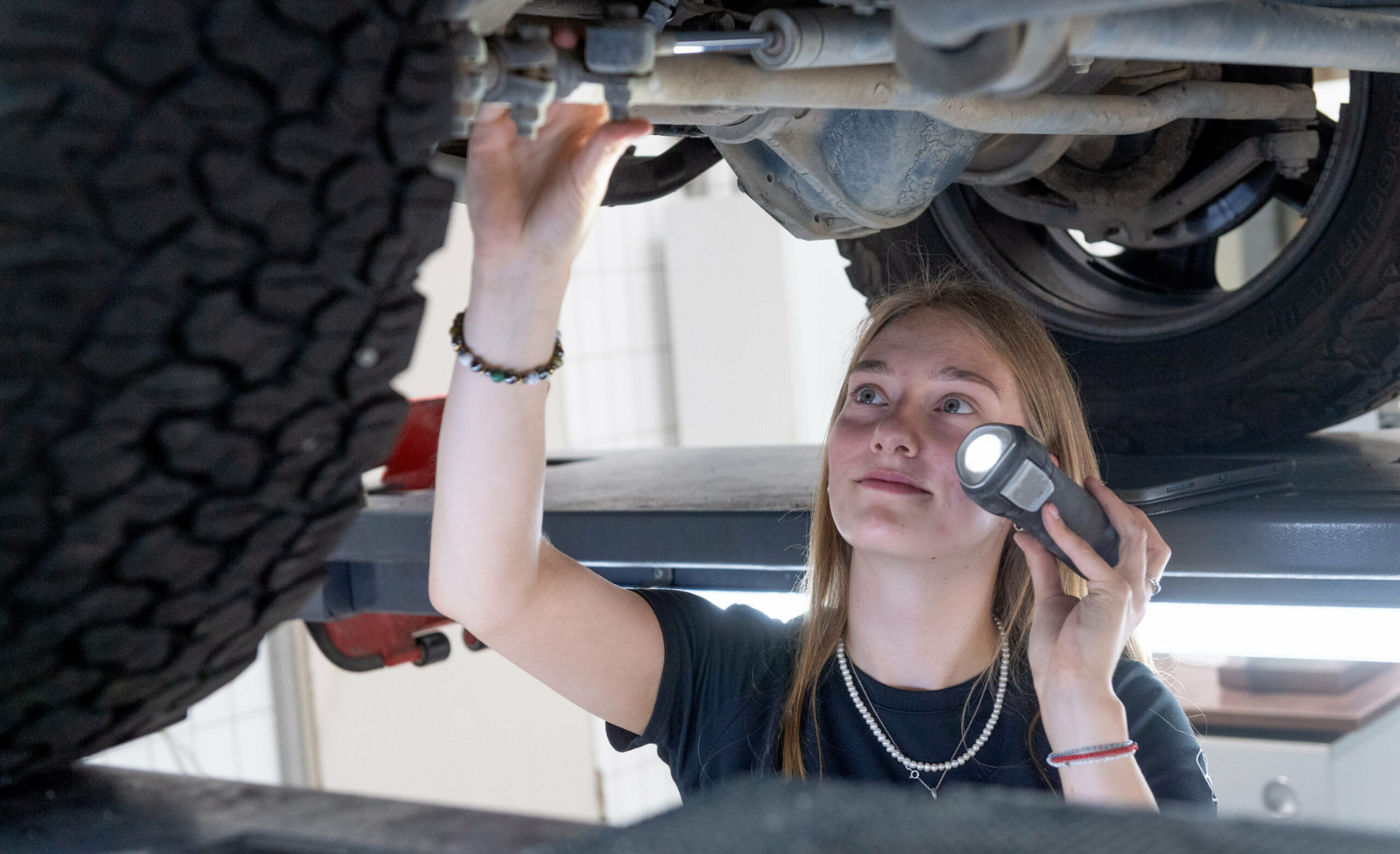 Melissa Schwab, Auszubildende zur Autmobilkauffrau bei Assenheimer + Mulfinger, untersucht in der Werkstatt die Unterseite eines Autos.