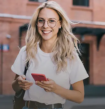 Frau mit Smartphone in der Hand schaut lächelnd nach vorne.