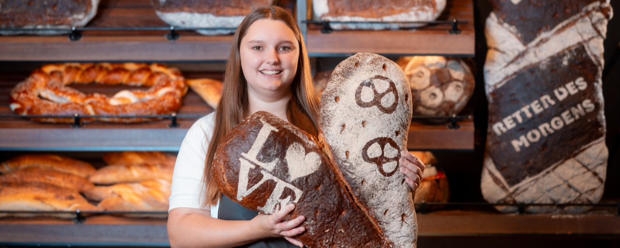 Mitarbeiterin hält lächelnd zwei Brote mit der Aufschrift Love und Bretzel in der Hand.
