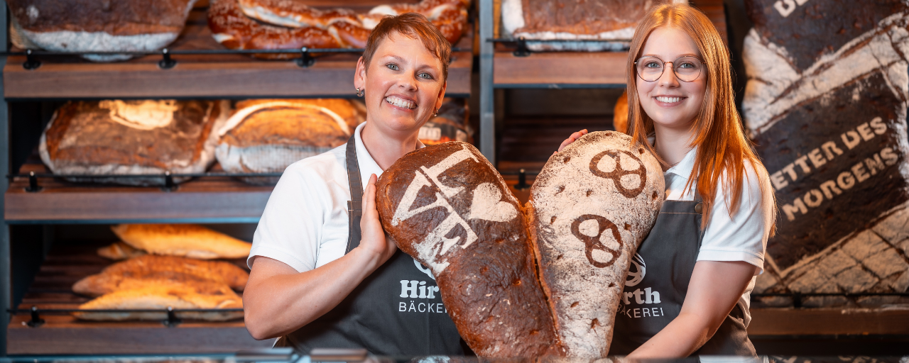Mitarbeiterinnen hält lächelnd zwei Brote mit der Aufschrift Love und Bretzel in der Hand.
