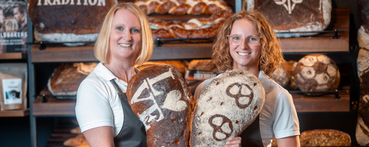 Mitarbeiterinnen hält lächelnd zwei Brote mit der Aufschrift Love und Bretzel in der Hand.