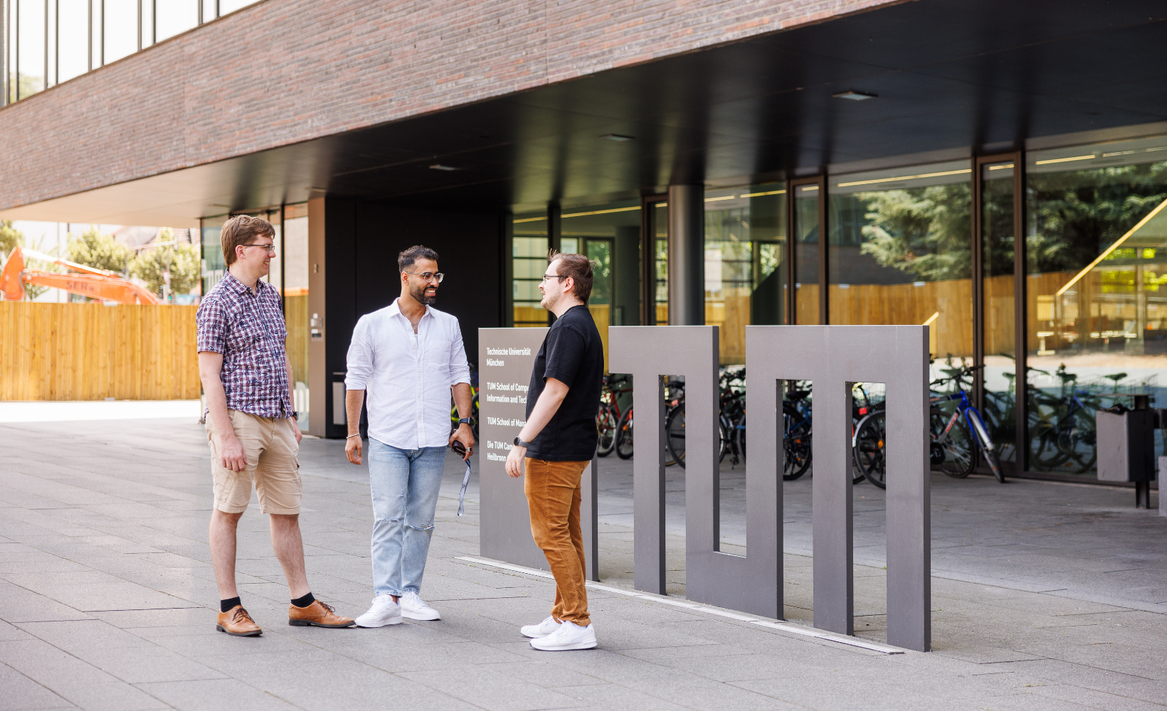 Drei Studenten stehen vor dem "TUM"-Schild und reden miteinander.